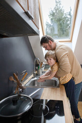 A boy with his father washes his hands on the sink