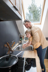 A boy with his father washes his hands on the sink