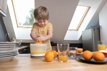 The boy squeezes orange juice in the kitchen by himself