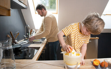 Kitchen Teamwork: Boy Squeezing Orange Juice While Father Cleans Up