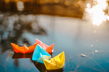 Multicolored paper boats. Colorful pink yellow blue orange ships in big spring snow puddle on...