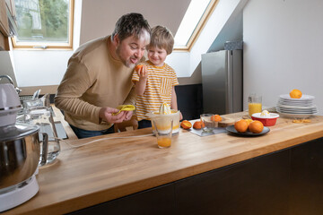 Fototapeta na wymiar The boy squeezes orange juice, and the father cleans up in the kitchen
