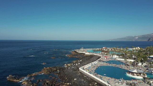 pictorial bird eye flight people relax on ocean beach with hotel swimming pools under boundless clear blue sky.