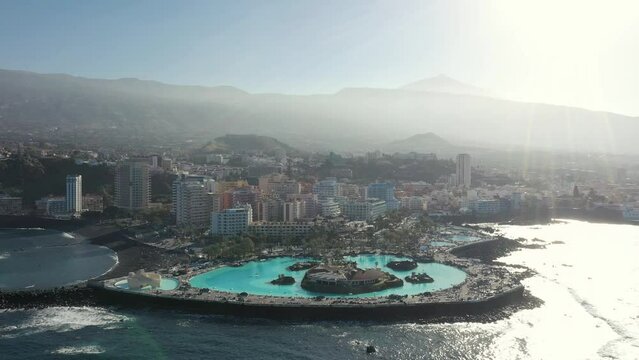 pictorial aerial panorama elite hotel with turquoise round swimming pool lying on peninsula against hills at sun rays.