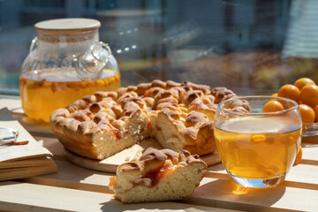 Homemade jam pie, tea in a glass teapot, a book and eyeglasses on the windowsill, home comfort concept.