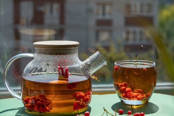 Tea with berries in a glass teapot on a window