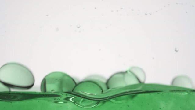 Macro shot of a lot of different sized green clear bubbles fall down to green surface bouncing and bursting on grey background | Background shot for cosmetics with green tea oil commercial