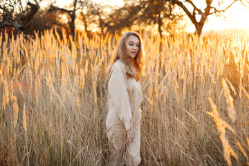 A gorgeous woman in an autumn field illuminated by the warm sun of an evening sunset. Golden ears of corn. Autumn