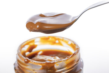 Close up of spoon scooping dulce de leche out of a jar, traditional sweet from Argentina isolated...