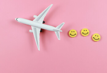 flat lay of airplane model with three yellow circle smiling faces  on pink  background. Happy or fun trip concept.