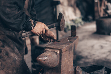 Blacksmith process metal with hammer on anvil in forge. Farrier in dirty clothes strike iron in workshop. Metalworking.