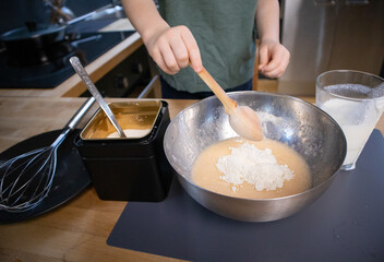 The boy prepares the dough from eggs, sugar, sour cream and flour by himself in the kitchen