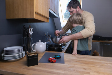 Father and son in the kitchen preparing batter for pancakes and cooking them.