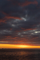 Naklejka na ściany i meble Bright orange sunset and thick clouds above the sea