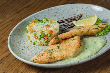 Chicken chops in batter with sauce in a plate with rice and vegetables