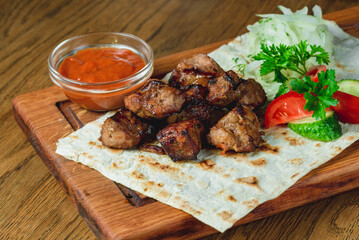 Baked pieces of shish kebab on pita bread with fresh vegetables and ketchup on a board