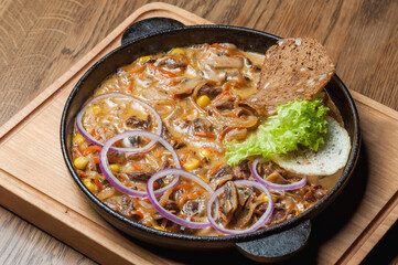 Baked meat with mushrooms, vegetables and greens in a pan on a board