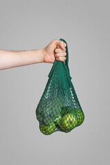 zero waste packaging.A shopping bag with green apples in a man's hand on a gray background
