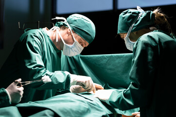 Surgeon operating on patient, team of medical professionals working in operating room, cropped shot in dark tone.
