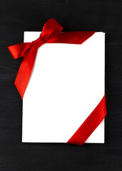 Top view of white holidays gift card with red bow on dark wooden background 