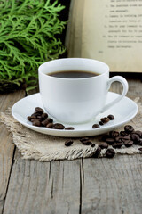 White cup of coffee with roasted coffee beans old book and thuja branches on wooden background