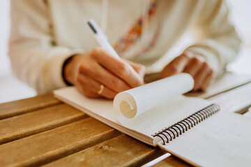 A man drawing sketches in sketchbook, paper is rolled, view of man's hands in white hoodie writing...