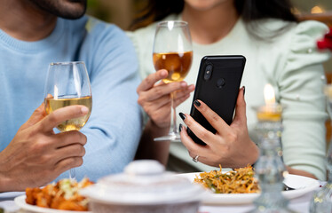 close up shot of couple hands using mobile phone by having drinks during candlelight dinner - concept of wedding anniversary celebration, cyberspace and dating application