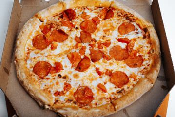 Fresh spicy pepperoni pizza with mozzarella, tomatoes, sauce in cardboard box. Italian food delivery