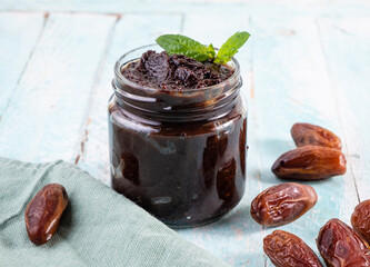 Useful date paste with cocoa in a glass jar on a wooden background, around the dates.