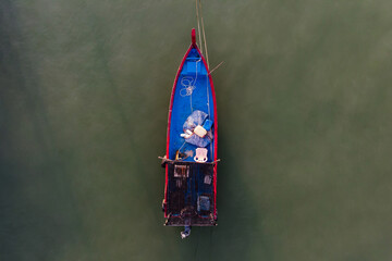 Aerial top down view of a blue & red colour fishing boat parked nearby the shore with isolated greenish colour sea water