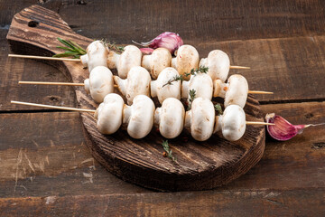 Wooden skewers with raw mushrooms on a wooden board.