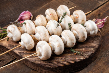 Skewers with raw mushrooms before cooking on a wooden background.