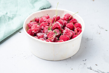 Frozen raspberries in a white paper eco dish, winterizing, gray background.