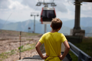 A boy in a yellow T-shirt looks at the cable car.