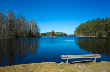 Picturesque Swedish nature, a wooden bench by a calm lake, blue sky reflecting in the water on a spring sunny day, Lake Snyten in Vastmanland, Sweden