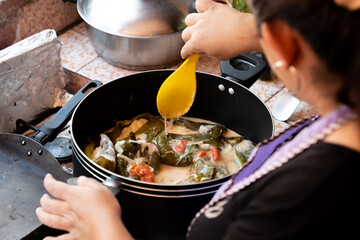 unrecognizable woman mixing with a wooden spoon homemade pepper stuffed with cheese and cream sauce, latin food