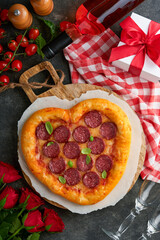 Valentines day heart shaped pizza with mozzarella, pepperoni and basil, wine bottle, two wineglass, gift box on black background. Idea for romantic dinner Valentines day. Top view. Mock up.