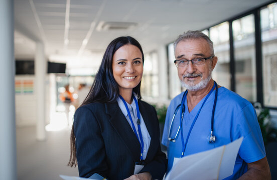 Portrait Of Elderly Doctor And Business Woman At Hospital Corridor.