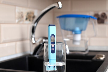 Tds meter for measuring water hardness is in the kitchen next to the sink, blue filter jug for water