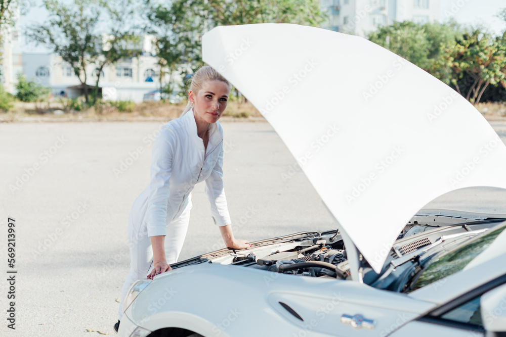 Wall mural a woman stands at the hood of a car repairing a car