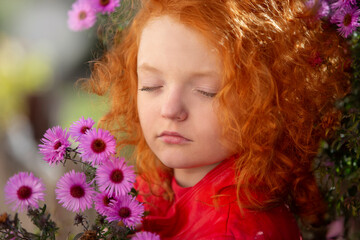Naklejka premium Red-haired little girl with closed eyes holds a bouquet of purple chrysanthemums.