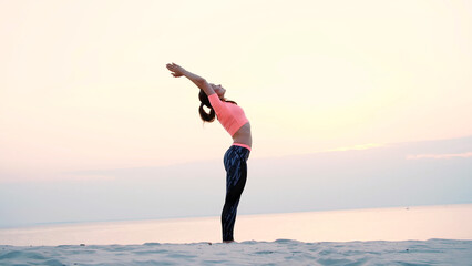 Healthy, young beautiful woman meditating, practicing yoga among the sand, on the beach, by the sea, river, at dawn, at sunrise, closeup