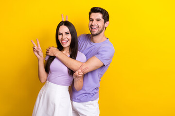 Obraz premium Photo of two idyllic positive carefree people hug show v-sign make horns isolated on yellow color background