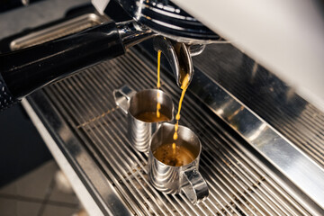 Espresso machine pours fresh black coffee closeup. Coffee machine preparing fresh coffee and pouring into yellow cups at restaurant, bar or pub.