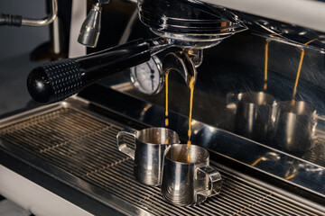 Fototapeta na wymiar Espresso machine pours fresh black coffee closeup. Coffee machine preparing fresh coffee and pouring into yellow cups at restaurant, bar or pub.