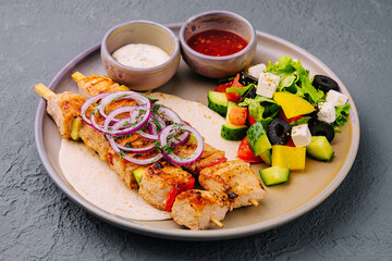 chicken skewers with greek salad and creamy, spicy sauces