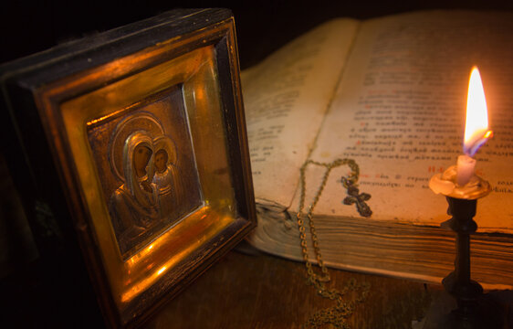 A candle illuminates the icon of the Virgin Mary and a cross on a chain lying on an open psalter