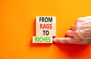 Rags or riches symbol. Concept words From rags to riches on wooden blocks. Beautiful orange table orange background. Businessman hand. Business rags or riches concept. Copy space.