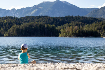 Fototapeta na wymiar kid boy preschooler child relaxing on fitness mat pebbles beach amazing lake view mountains background.blue turquoise color water.happy child enjoy summer time no clothes sunshine on body relax 