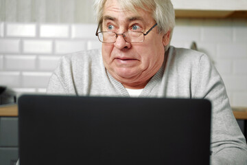 Senior grey haired man wearing glasses sitting at laptop and making fish face with lips. Crazy and comical gesture. Funny Old grandfather with playful silly facial expression grimacing fooling around